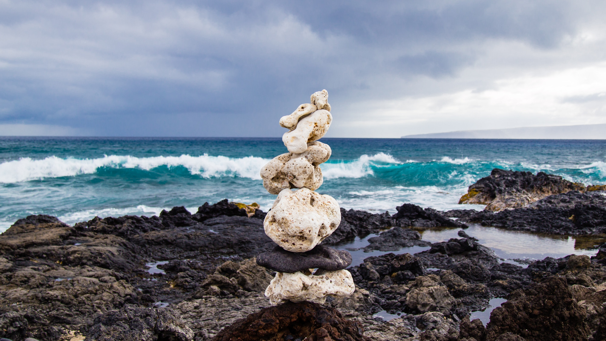 Medium sized stones are piled up to form a tower on a rocky shore in front of the sea.